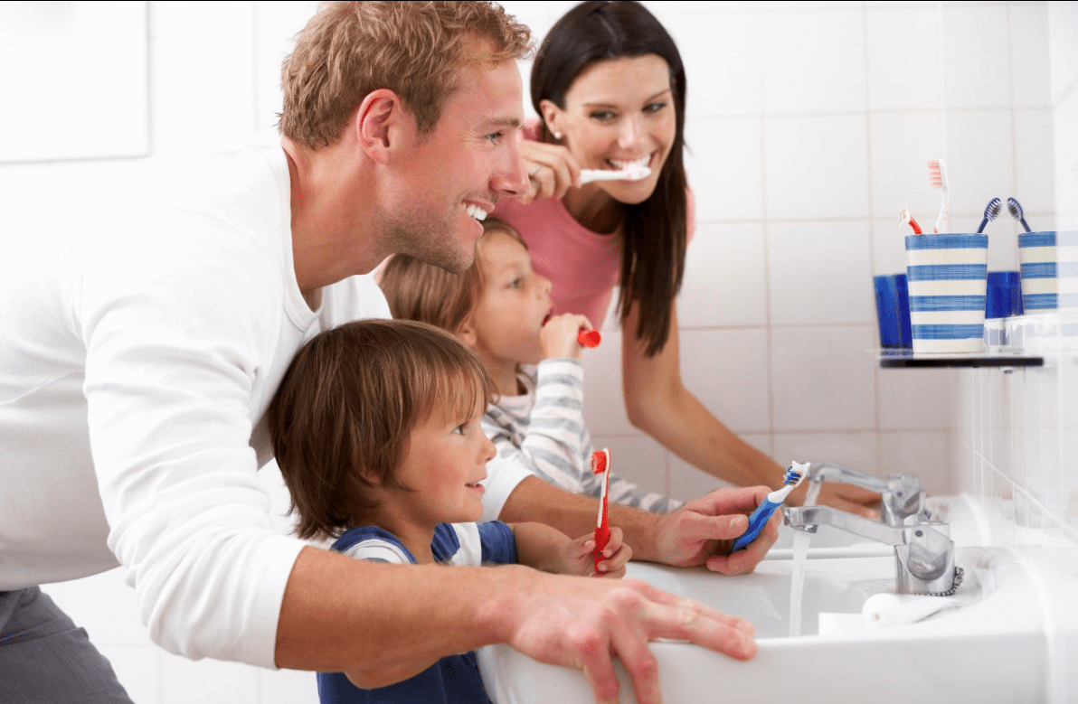 Two adults to children at sink brushing teeth