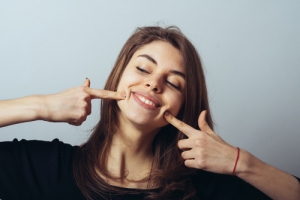 Young woman pointing at her smile with both hands