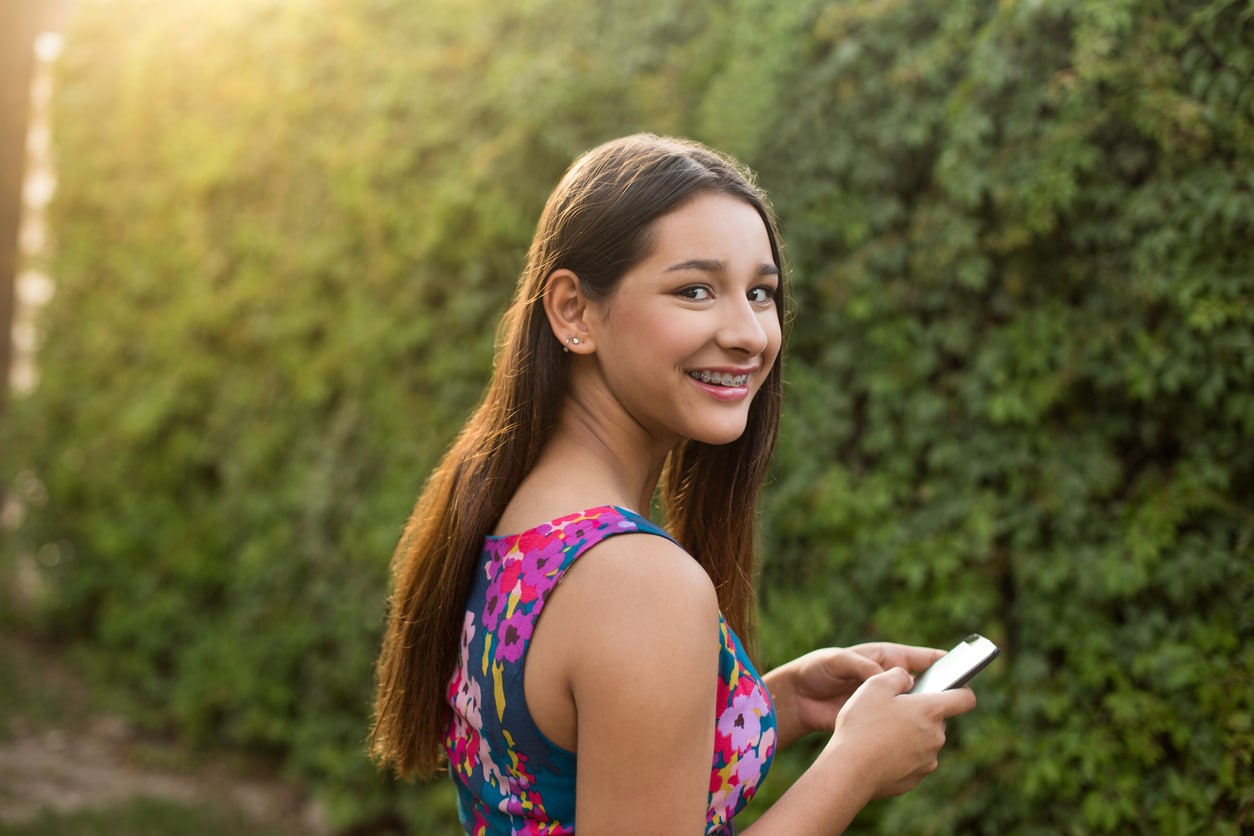 Teenage girl texting, smiling and looking at camera