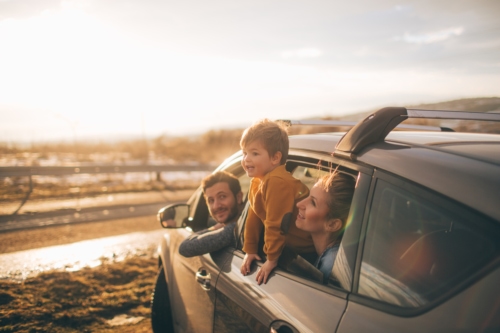 Young child hanging out car window with family