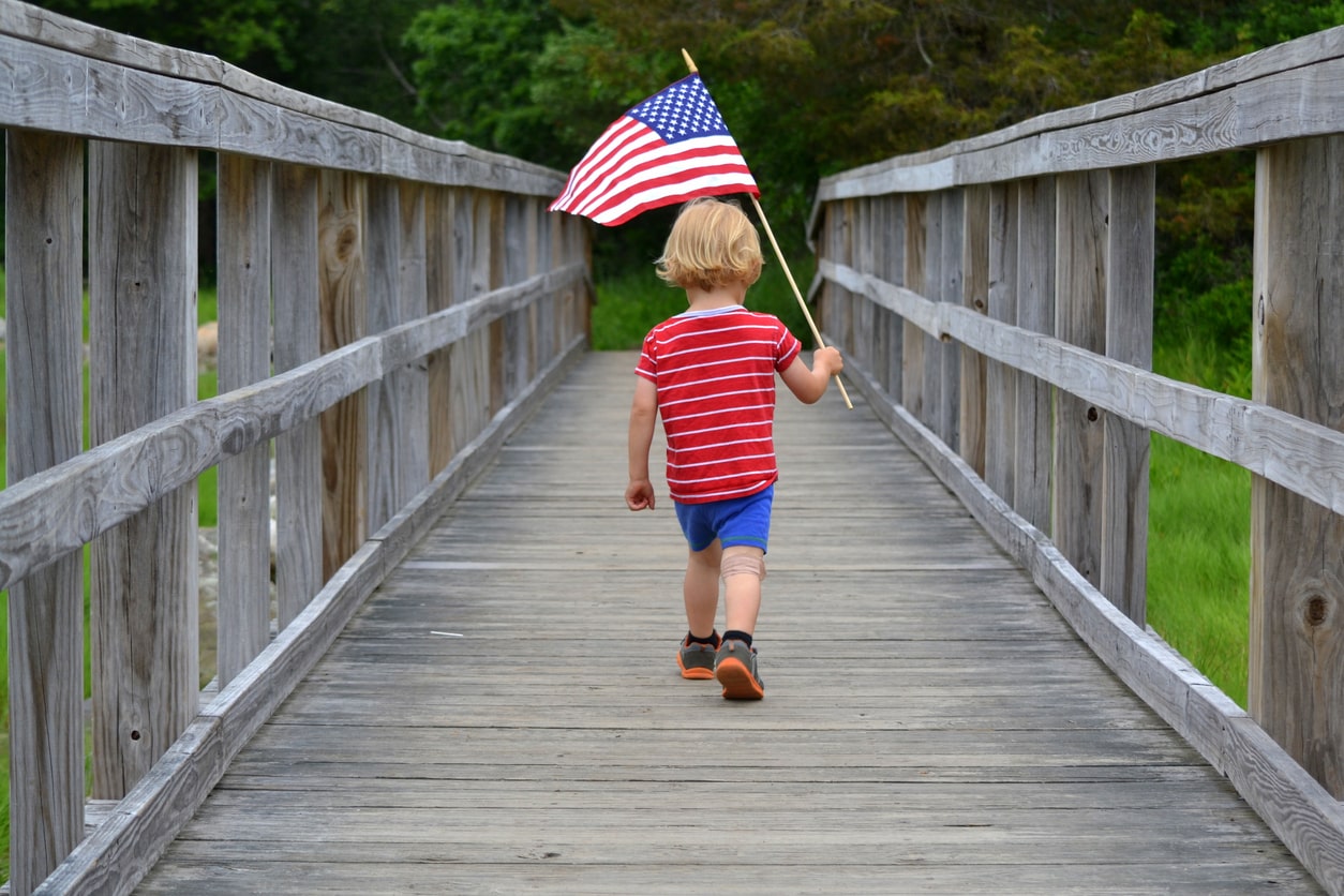 Young boy holding American flag on wood bridge