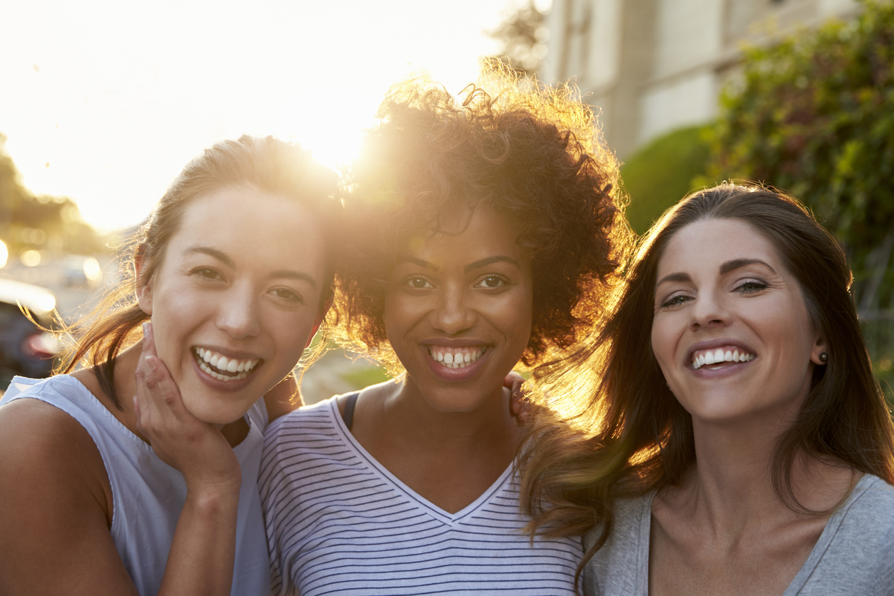 Group of three adult women looking at camera smiling in sun